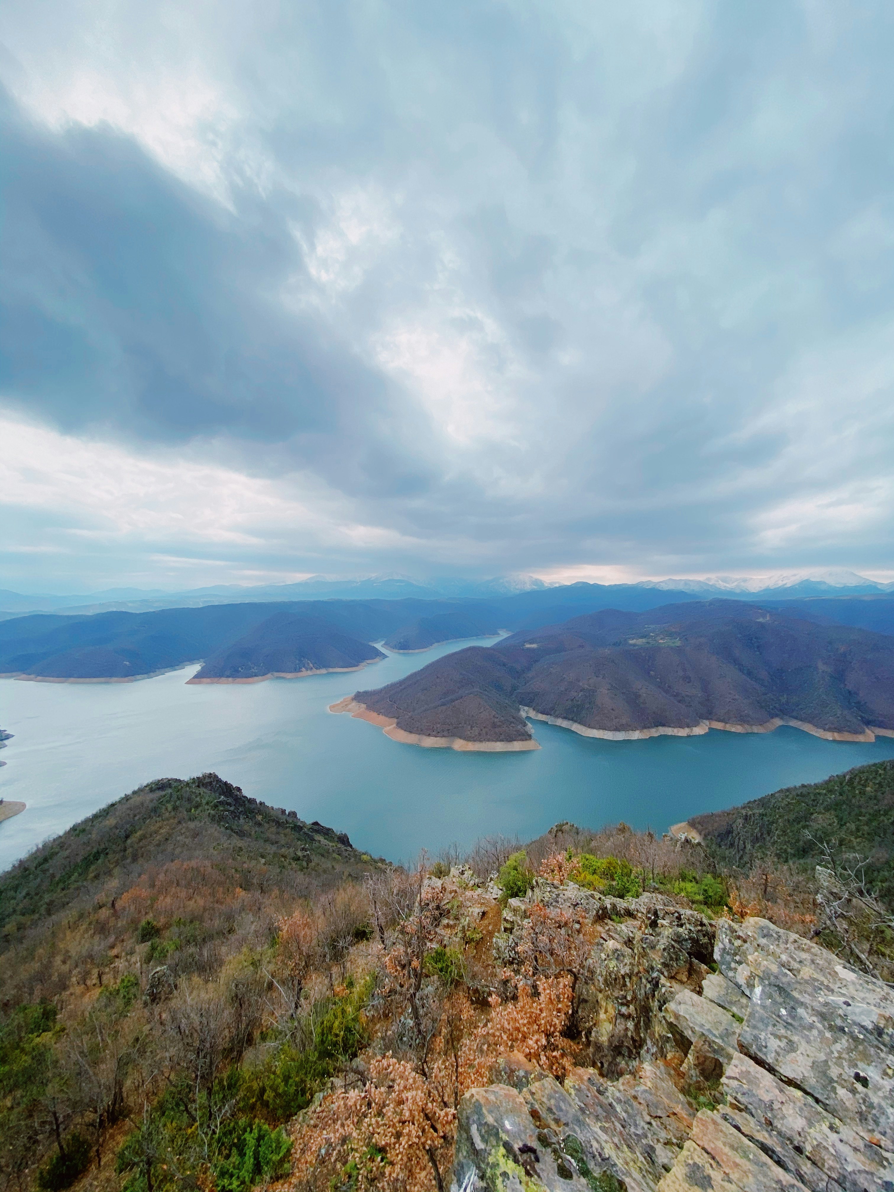 green and brown mountain near body of water under white clouds during daytime